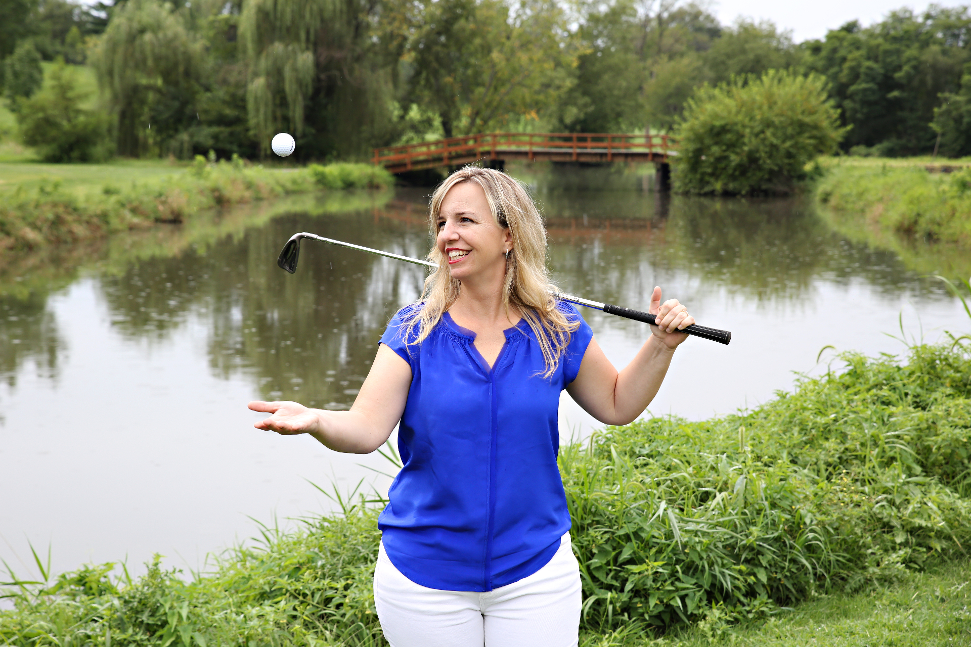 Allison George, Founder & Wizard of Fun, smiling on a golf course with a club over her shoulder